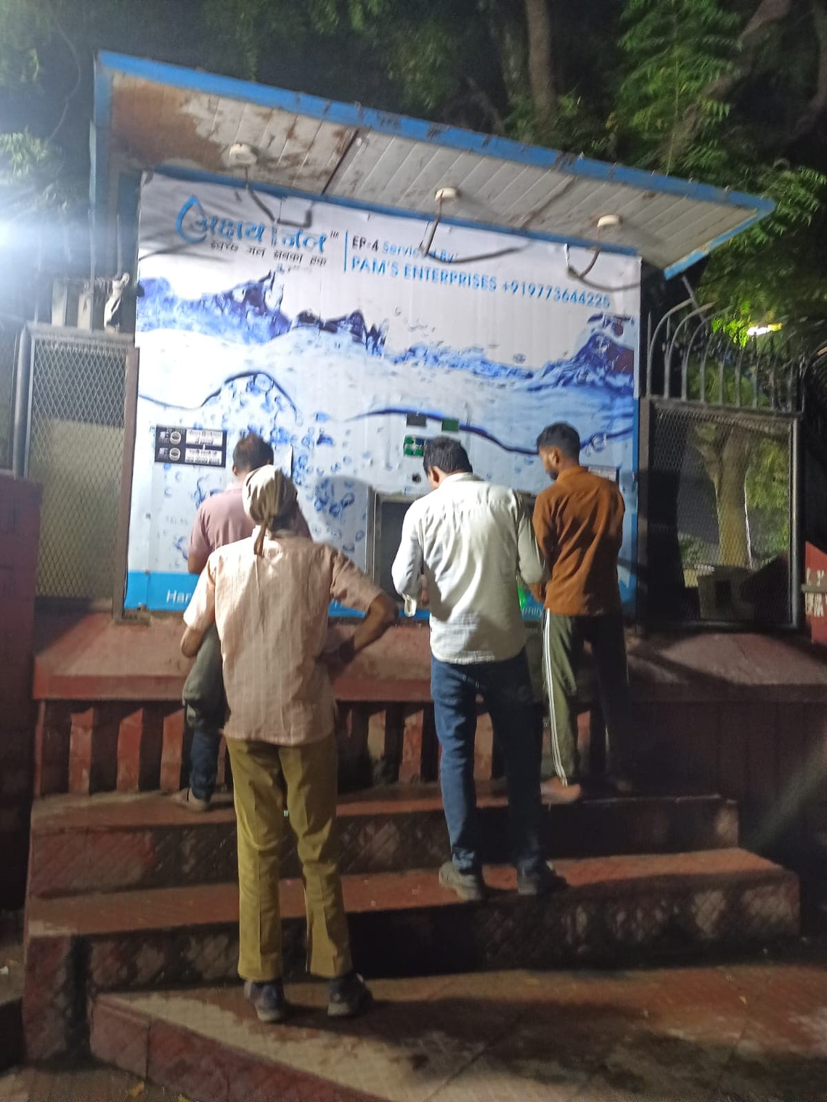 Maintenance engineers checking a kiosk's smart interface on a tablet at an urban transit hub at night